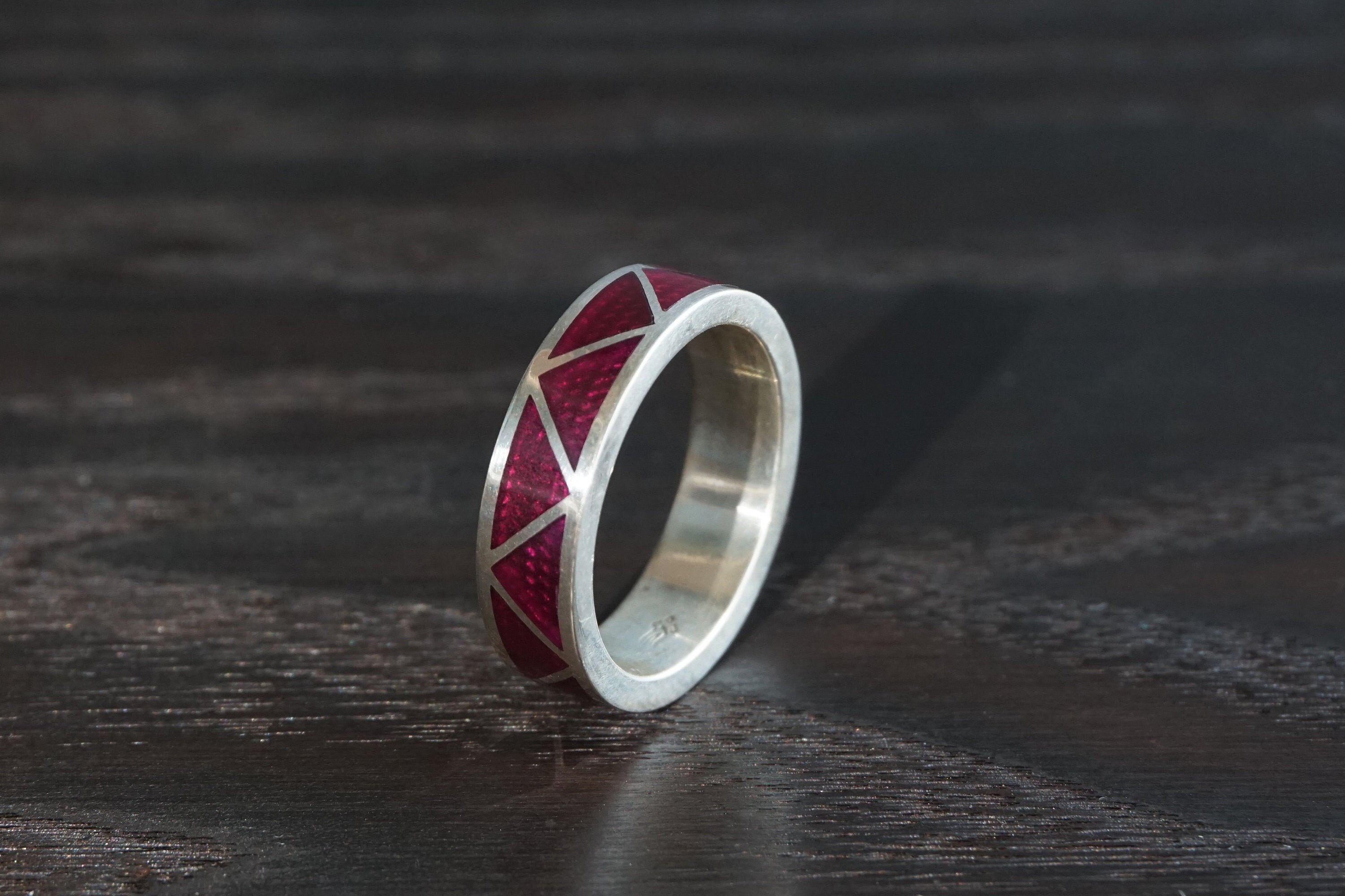 Silver ring with red geometric design on a dark wooden surface