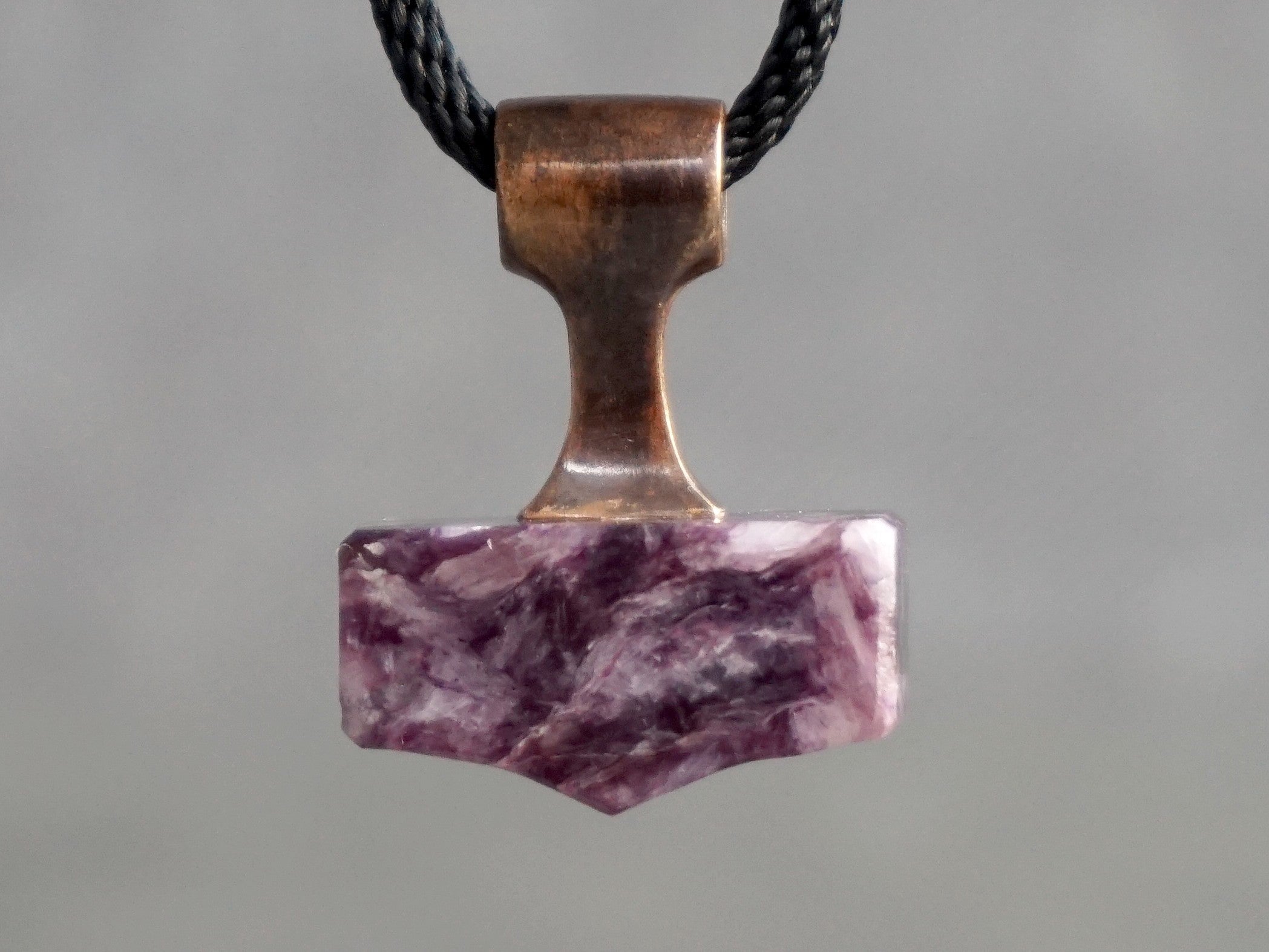 small hammer amulet made of bronze and purple stone with wavelike pattern