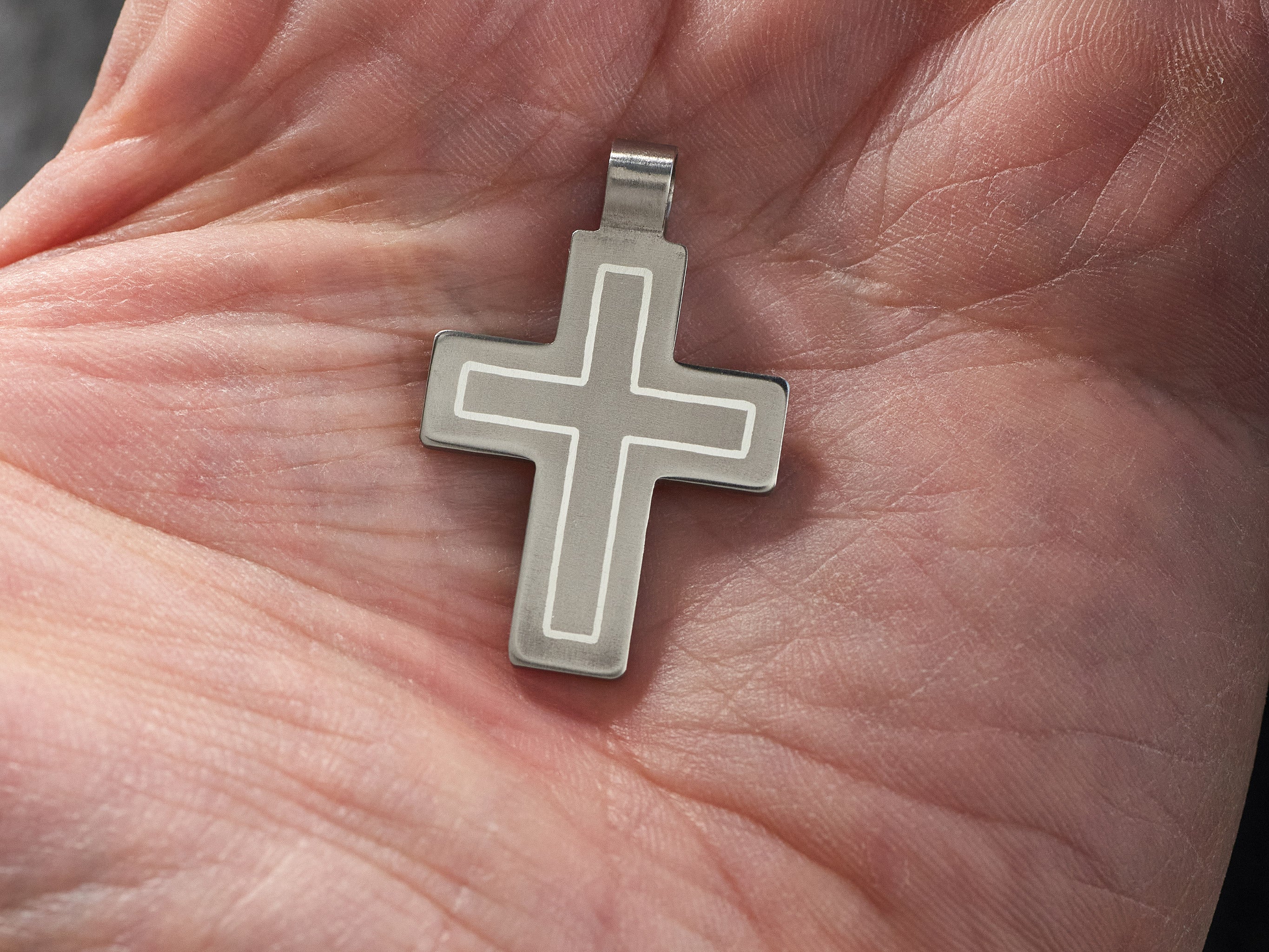 titanium cross pendant worn on hand showing scale and real size