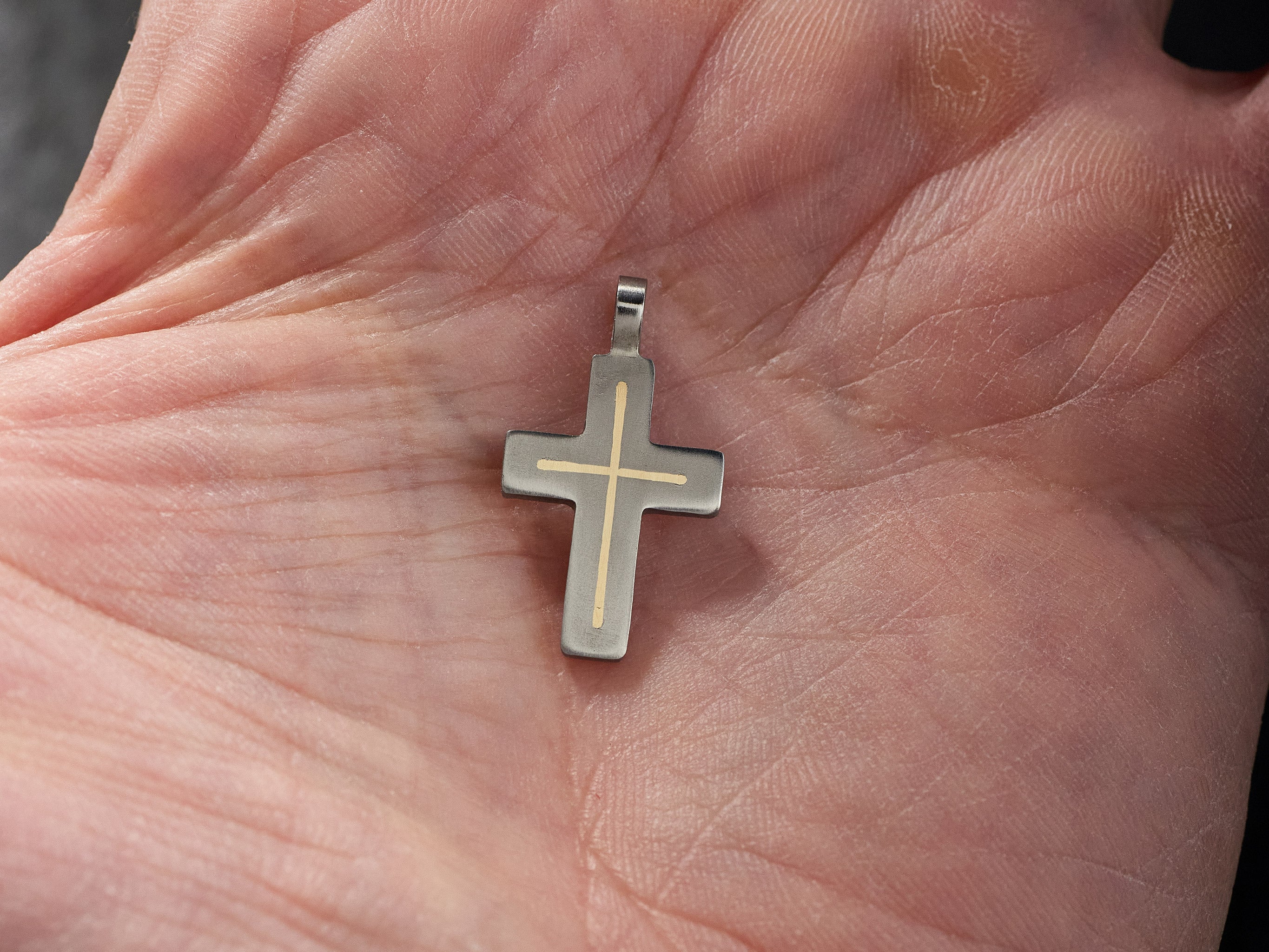 Small handmade titanium cross pendant worn on hand showing scale and minimalist style