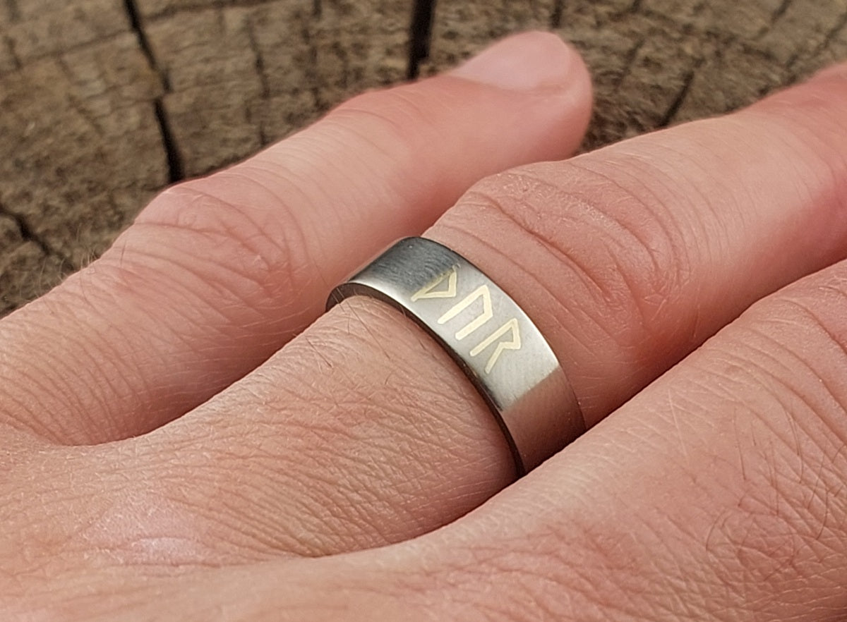 Handmade titanium Thor rune ring worn on a finger, featuring Younger Futhark silver inlay and satin brushed finish.